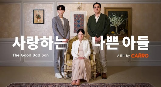 The video thumbnail shows a formal portrait of a three-person family unit against an ornate background. A man and a young man stand on either side of a woman who is seated on a chair. The woman is wearing a light-colored outfit, while the men are dressed in formal attire. The image is titled in large Korean characters and smaller English text: "사랑하는 나쁜 아들" (Saranghaneun Nappeun Adeul), which translates to "The Good Bad Son," and is listed as "A film by CARRO".