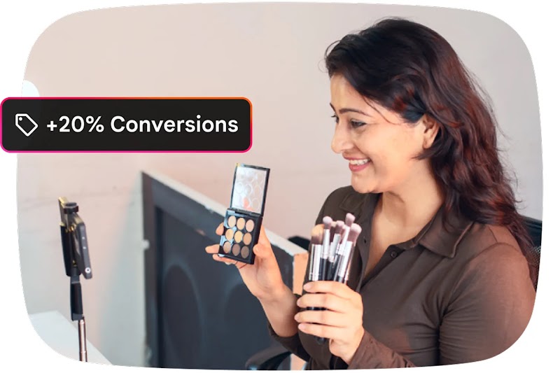 A smiling woman films a makeup tutorial with a smartphone on a tripod, holding up an eyeshadow palette and brushes. A black text overlay in the corner reads: "+20% Conversions”.