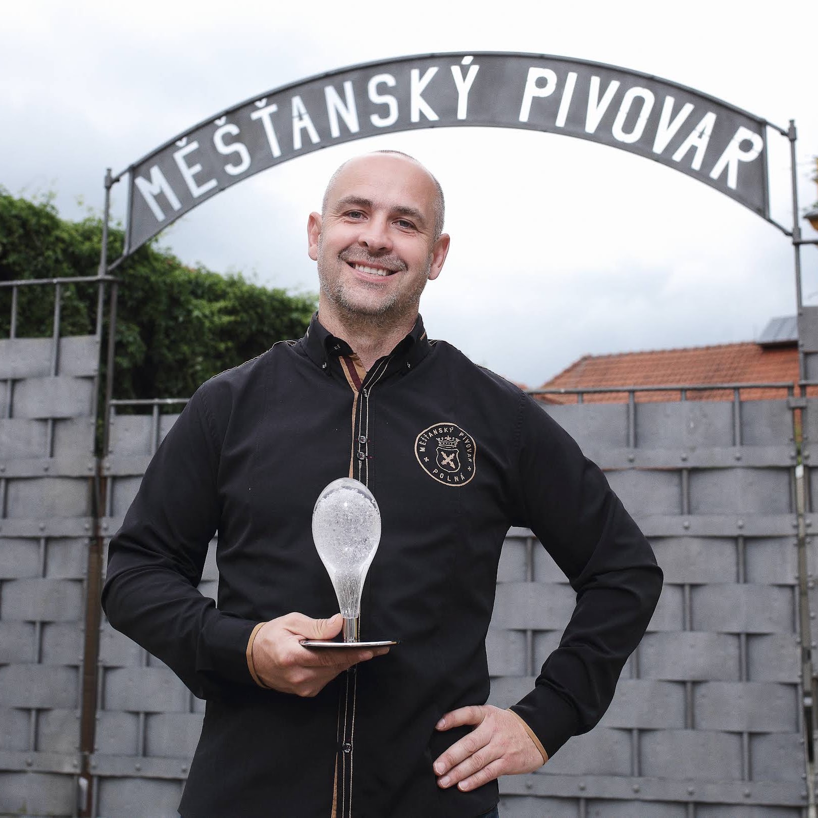 Ladislav Pártl, spolumajitel Měšťanského pivovaru Polná, stojí před bránou s nápisem Měšťasnký pivovar a drží ocenění Křišťálový špendlík.