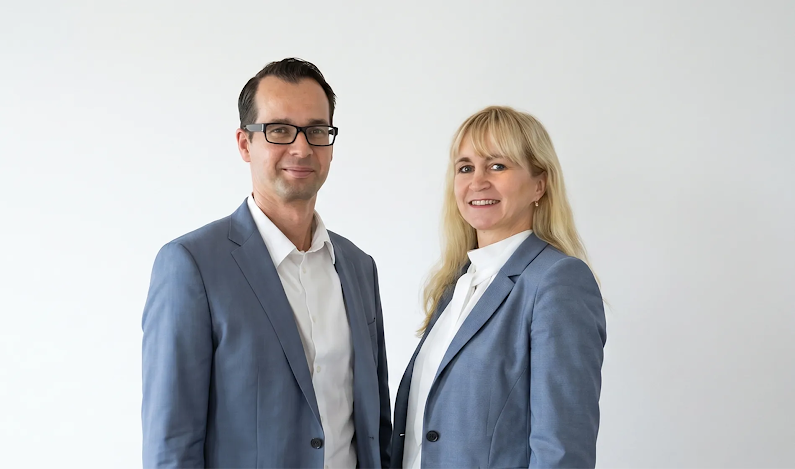 Ein Mann und eine Frau im Anzug vor ihrem Firmenlogo
