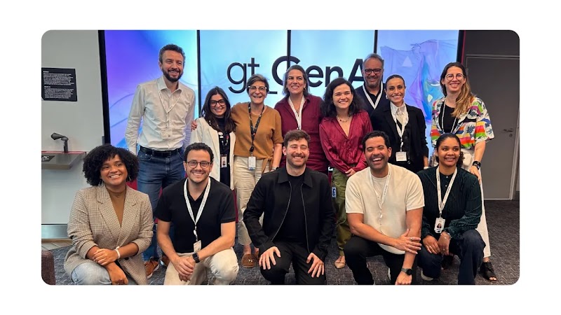 Participantes do gt_GenAI - 2º encontro, reunidos à frente de um painel luminoso.  Na fileira de trás, estão de pé, da esquerda para a direita Andre Kliousoff, Anna Júlia Gelain, Monica de Carvalho, Marina Tunes, Amanda Agapito, Daniel Deivisson, Andressa
