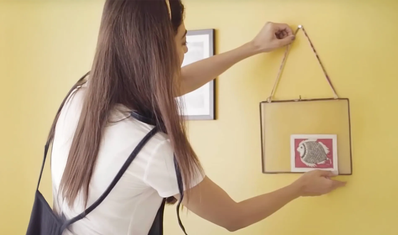 A woman hanging a decor on a yellow painted wall