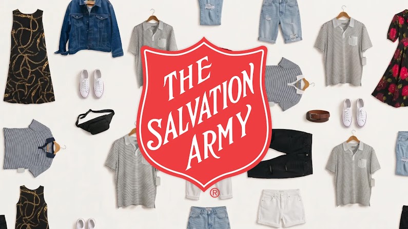 The red and white Salvation Army shield emblem appears against a white background with gray, black, red, and white articles of clothing, including dresses, pants, tops, and shoes, laid flat.