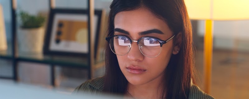 Una mujer morena de pelo lacio y anteojos mira la pantalla de un computador.