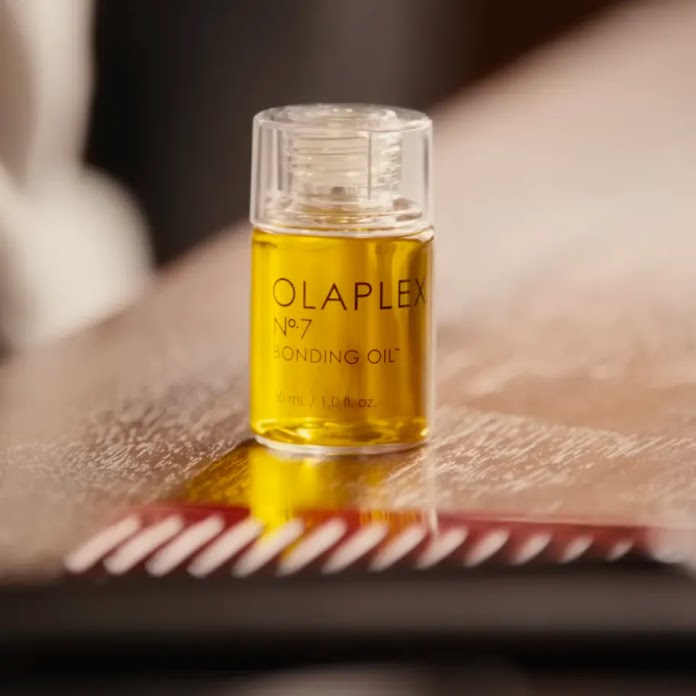 A small bottle of golden Olaplex No. 7 Bonding Oil sitting on a polished surface.