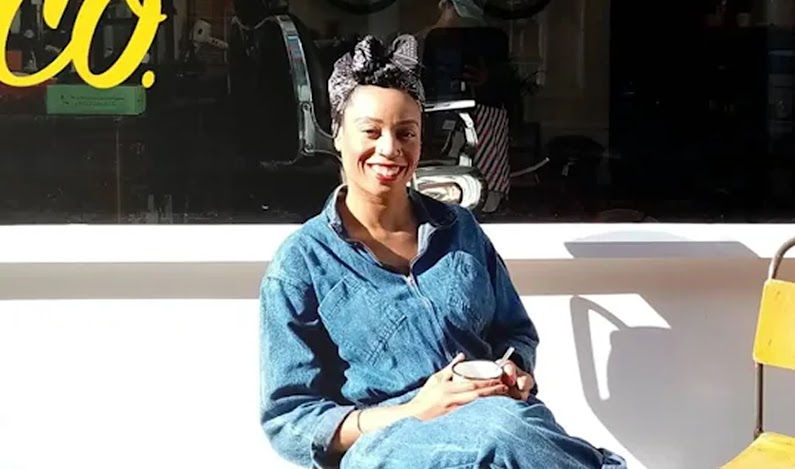 Owner of Levy & Co sits in front of a cafe with a mug of coffee.