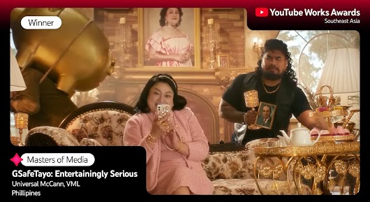 A man and woman in an ornately decorated, luxurious room. The woman is seated, looking at her phone, and the man stands behind a gold tea-set tray, holding a small framed photo and a chalice. A large portrait hangs on the wall behind them. The overlay text reads: "Winner," "Masters of Media," "GSafeTayo: Entertainingly Serious," and "Universal McCann, VML | Philippines."