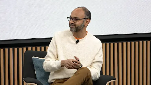 Harikesh Nair, Senior Director of Data Science and Engineering bei Google, sitzt während einer Podiumsdiskussion in einem Sessel. Er hat kurzes, dunkles Haar, einen Bart und trägt einen cremefarbenen Pullover.