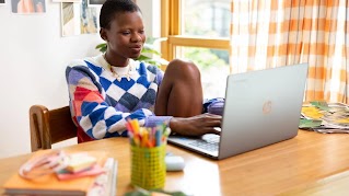 A young professional sits at a desk, focused on her laptop in a bright, modern office space.