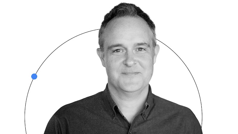 Michael Bailey, director senior de Google Media Lab, posa sonriente en su retrato. Tiene el pelo corto y los ojos y la piel claros, y lleva una camisa de color oscuro. Alrededor de su retrato se ve una fina línea negra con un punto azul.