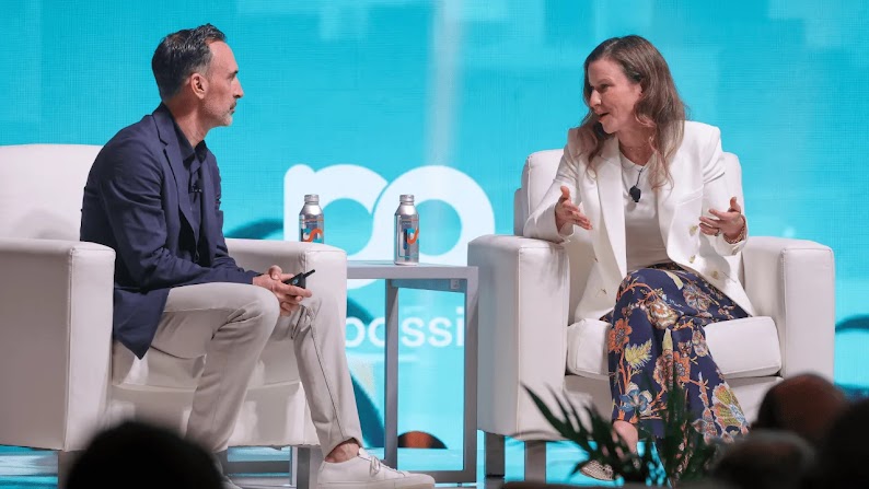 Sean Downey, president, Americas & Global Partners, Google, sits across from Laura Jones, CMO of Instacart, on the stage at Possible Miami in front of a teal and green background, decorated with a city skyline and palm trees.