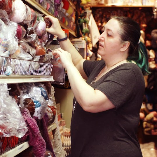 Зображення власника компанії Cook’s Arts & Crafts, який дістає нитки з полиці