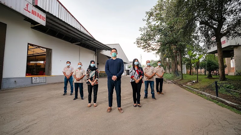 Sebuah tim berdiri bersama di luar fasilitas manufaktur mereka