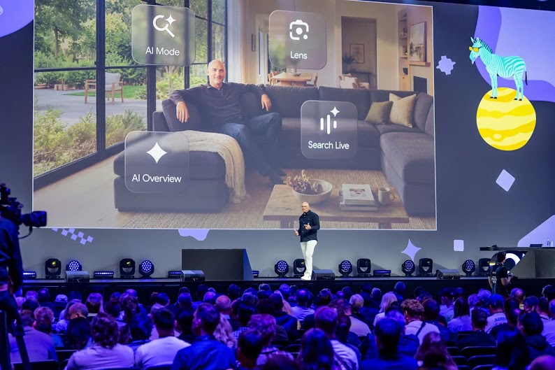 Brendon Kraham, VP of Global Search Ads & Commerce bei Google, spricht auf der Bühne der OMR. Ein großer Bildschirm hinter ihm zeigt einen Mann auf einem Sofa mit UI-Icons für AI Mode, Lens, AI Overview und Search Live. Im Vordergrund sitzt das Publikum.