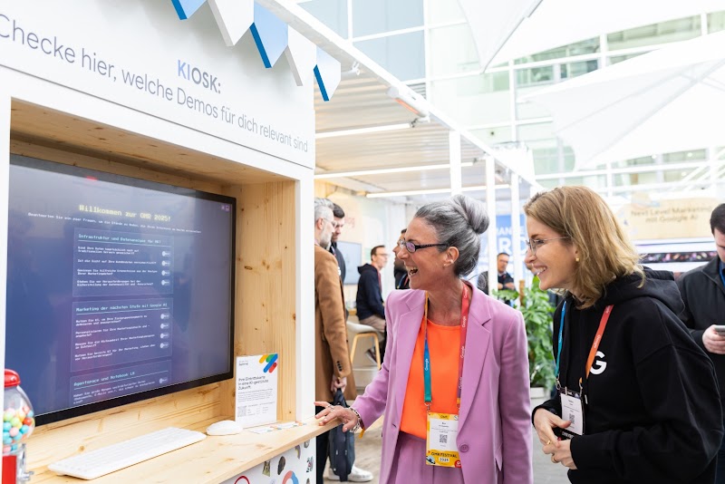 Zwei Personen stehen vor dem Google Haus Kiosk und interagieren mit ihm.