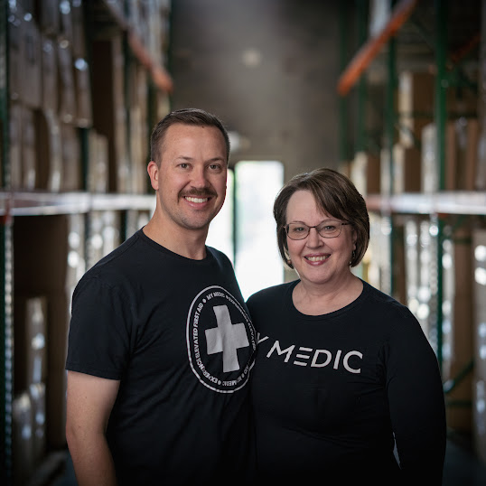 Landon Udy and his mother JoLynn Udy of My Medic wearing branded company t-shirts stand in a fully-stocked warehouse. 