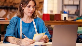 Una mujer, propietaria de una pequeña empresa, está sentada en un escritorio configurando una cuenta de Google Ads en su ordenador portátil.
