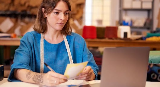 Una mujer, propietaria de una pequeña empresa, está sentada en un escritorio configurando una cuenta de Google Ads en su ordenador portátil.