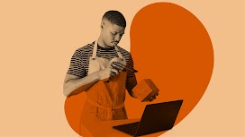 Um homem negro usando um avental de trabalho sobre uma camisa listrada aponta um leitor para o código de barras de um produto.