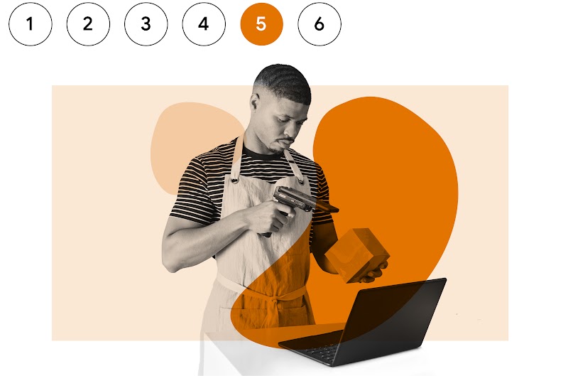 Um homem negro usando um avental de trabalho sobre uma camisa listrada aponta um leitor para o código de barras de um produto.