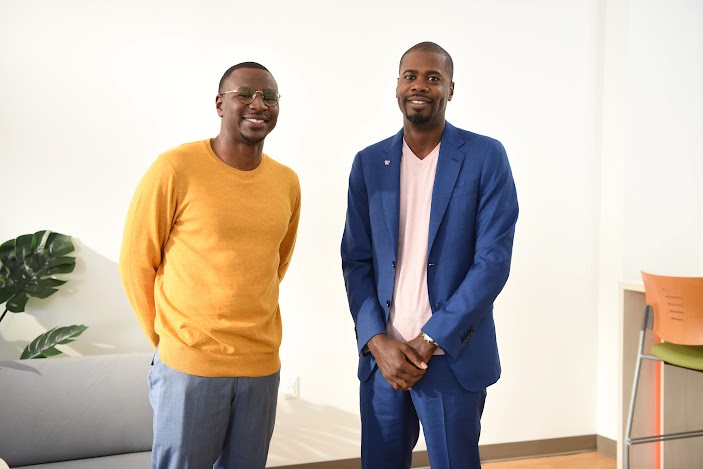 Randy D. Williams, Founder and CEO of Talley and Twine, wearing a blue blazer and light pink v-neck shirt, stands next to a colleague in a yellow sweater, both smiling at the camera in a bright, modern office.