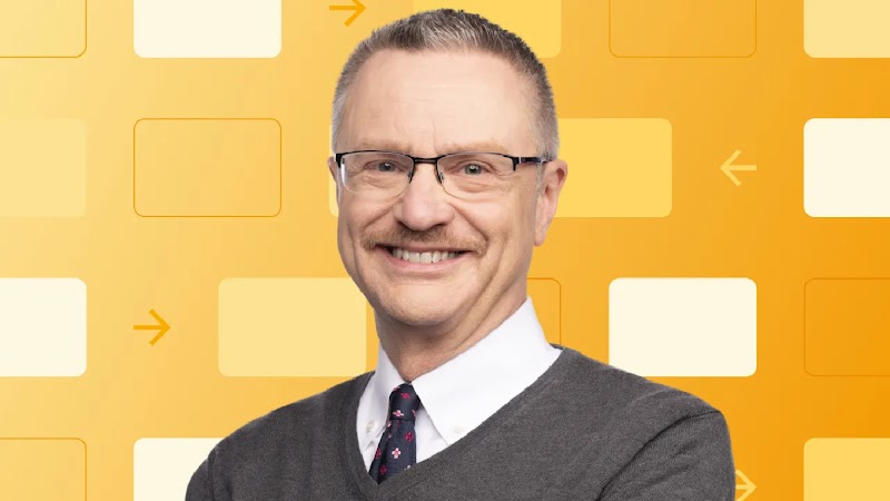 Se muestra al profesor y autor Jim Lecinski, sonriendo. Lecinski tiene el cabello de longitud media, ojos y piel claros, y usa gafas y un suéter con una camisa de cuello y corbata. Detrás de él se muestra el flujo de trabajo de un sistema
