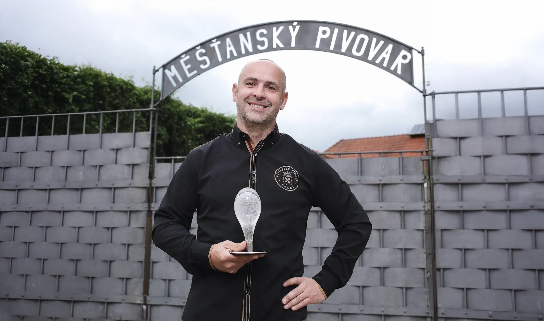Ladislav Pártl, spolumajitel Měšťanského pivovaru Polná, stojí před bránou s nápisem Měšťasnký pivovar a drží ocenění Křišťálový špendlík.