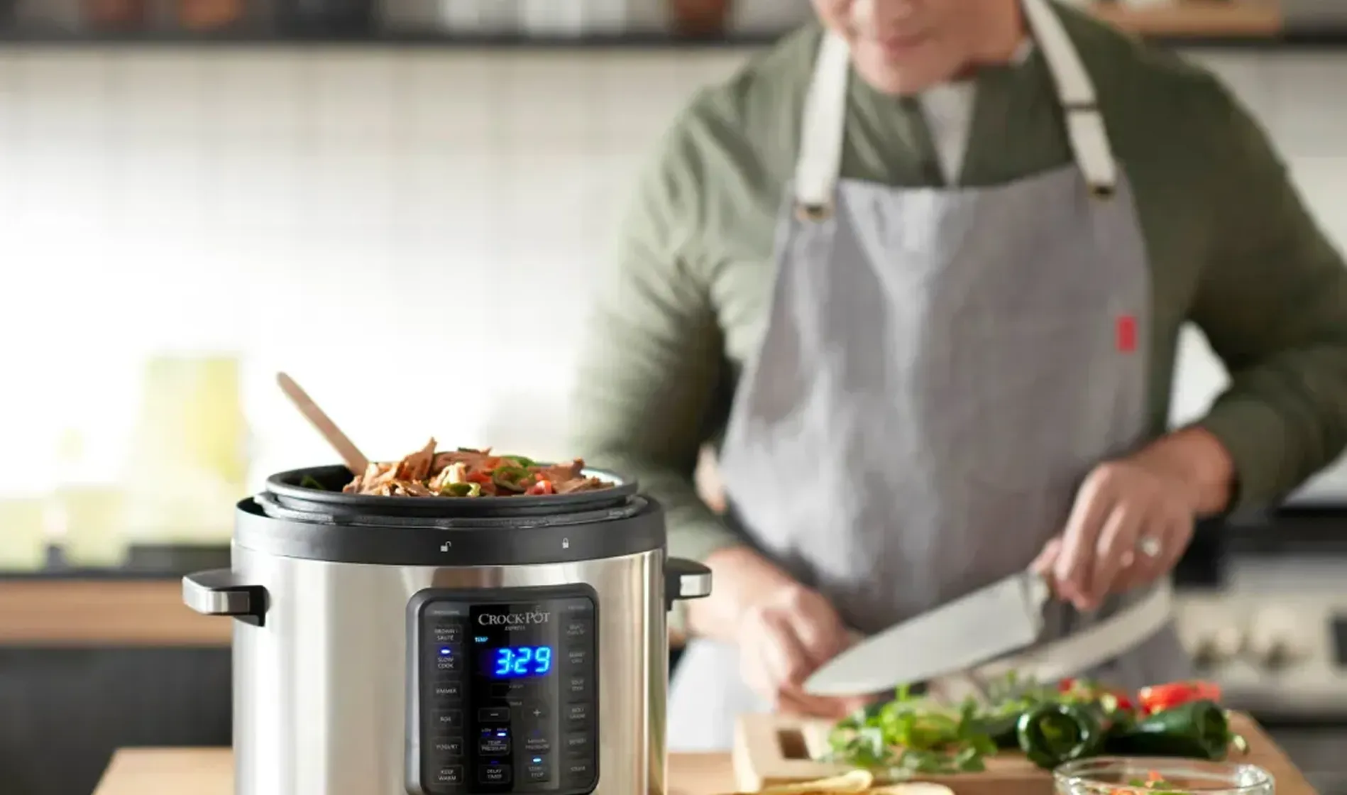 Un chef con delantal cocina con una olla inteligente de cocción lenta en primer plano.