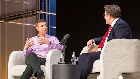 Google SVP Nick Fox sits on a stage in an armchair and talks with Ben Smith, editor-in-chief of Semafor. Smith wears a dark suit and red tie. Fox wears a pink collared shirt and dark slacks. Both have light skin and short dark hair.