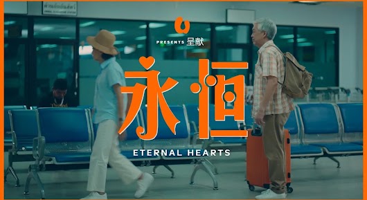 A cinematic video thumbnail showing an older man with luggage standing in a terminal waiting area, with large orange text that reads "永恒" and "ETERNAL HEARTS".