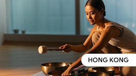 Hong Kong. A woman holding a mallet in one hand as she reaches out for one of the many Tibetan singing bowls before her.
