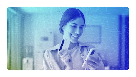 Mulher de cabelos escuros sorrindo e fazendo uma transação no celular, com o cartão em mãos.