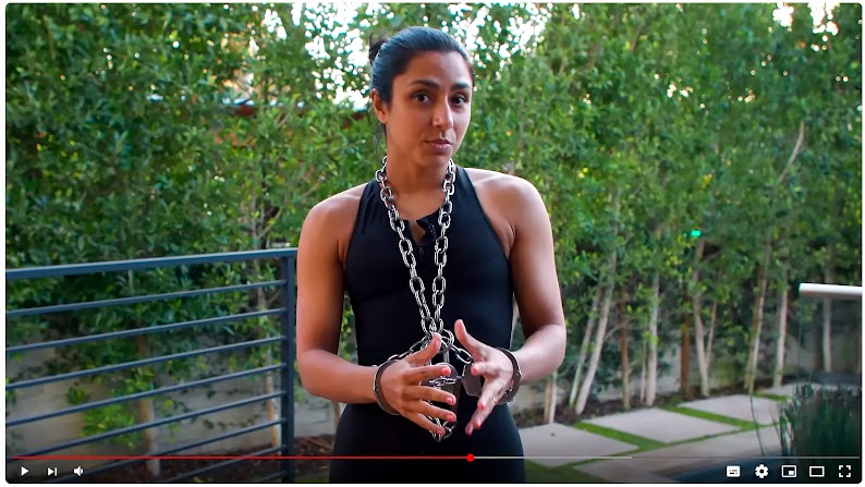 In a paused YouTube video, creator Michelle Khare stands in front of a row of trees and explains Houdini’s deadliest trick. She wears handcuffs and a thick chain around her neck