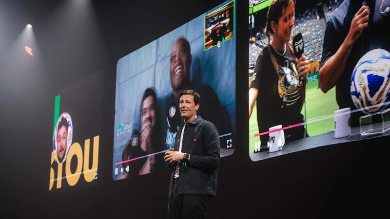 Harry Walker de pie en el escenario del YouTube Festival de fondo negro, con pantalones negros y chaqueta oscura, con tres grandes pantallas de vídeo detrás que muestran vídeos de varios creadores de contenido.