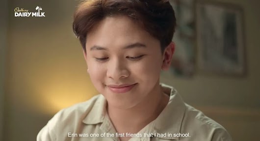 A Cadbury Dairy Milk video frame of a smiling young man looking down, with a subtitle reading 'Erin was one of the first friends that I had in school