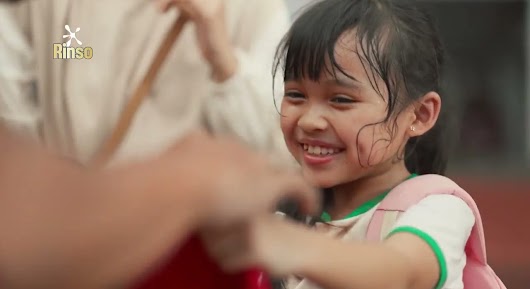 A video thumbnail for Rinso showing a smiling, slightly sweaty young girl with a pink backpack interacting with an adult.