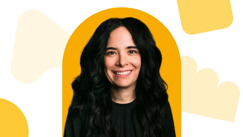 AMC Networks CMO Kim Granito appears in front of a yellow abstract background. Granito has long dark hair and eyes, light skin, and wears a black long-sleeve top.