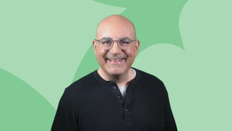 Shelly Palmer, CEO of The Palmer Group and advanced media professor in residence at Syracuse Univ. smiles at the camera, wearing a black pullover and glasses. He has light skin and a shaved head.