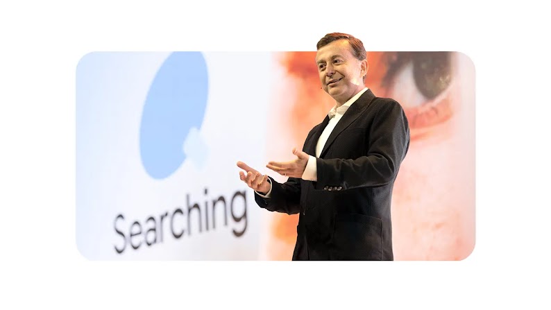 Fábio Coelho, presidente do Google Brasil, usa terno escuro e está sorrindo na foto. Atrás dele, um telão com a palavra ‘Searching’ está em destaque.