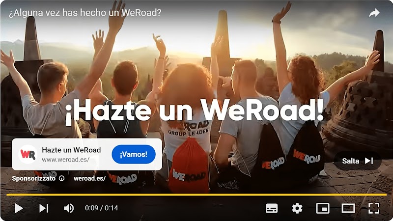 Vediamo un'immagine di una pubblicità su YouTube che mostra un gruppo di cinque giovani di spalle, gioiosi con le braccia alzate, al tramonto in un antico complesso di templi con cupole.