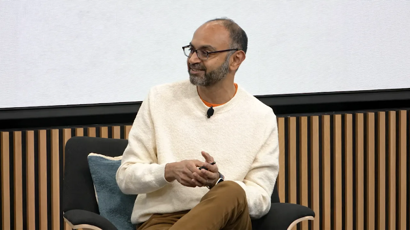 Harikesh Nair, senior director of data science and engineering at Google, sits in a chair while speaking on a panel. Nair has medium skin, short dark hair and beard, and wears a cream pullover sweater.
