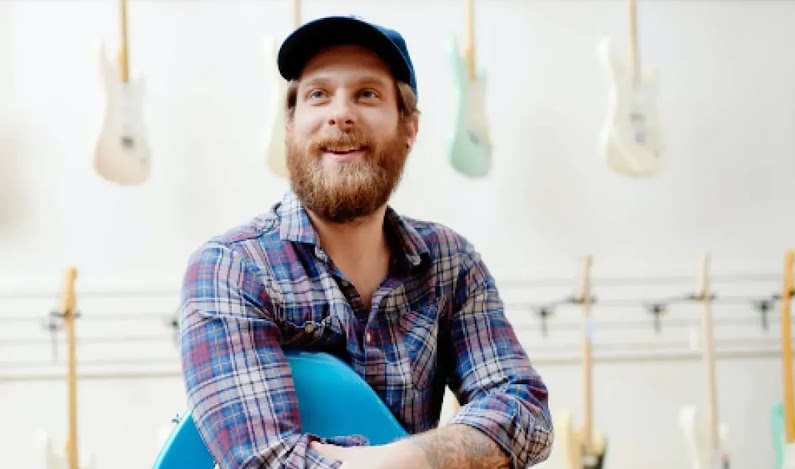 Owner of Chicago Music Exchange looks beyond in front of a wall of guitars.
