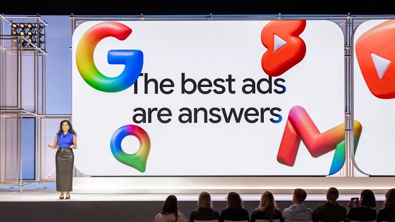 Google-Managerin Vidhya Srinivasan spricht von der Bühne der Google Marketing Live. Ein großer Bildschirm hinter ihr zeigt eine Präsentation mit dem Titel „The best ads are answers“. Google-Logos schweben wie Luftballons um die Worte herum.