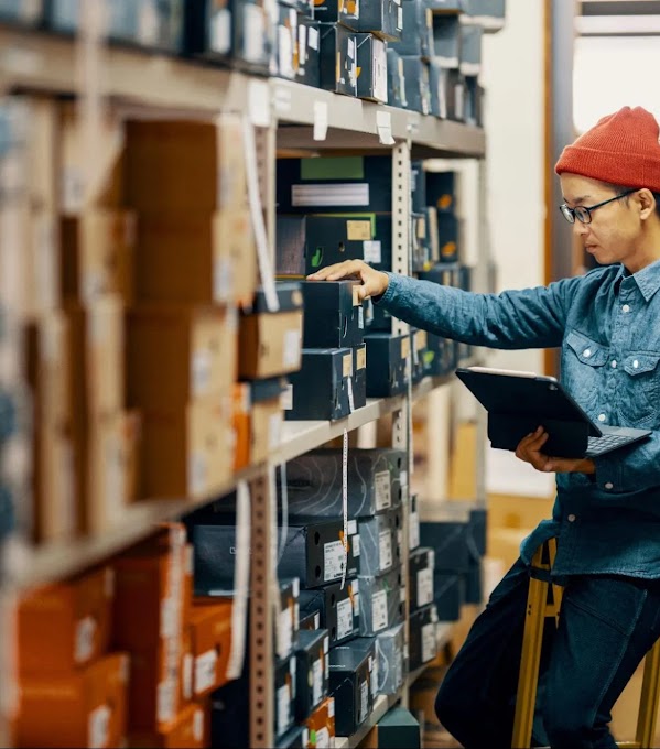 A retail worker manages their store inventory, looking through shelves with laptop in hand.