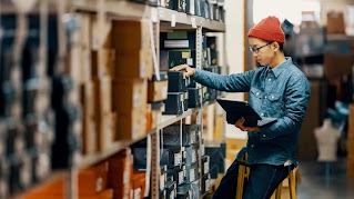 A retail worker manages their store inventory, looking through shelves with laptop in hand.