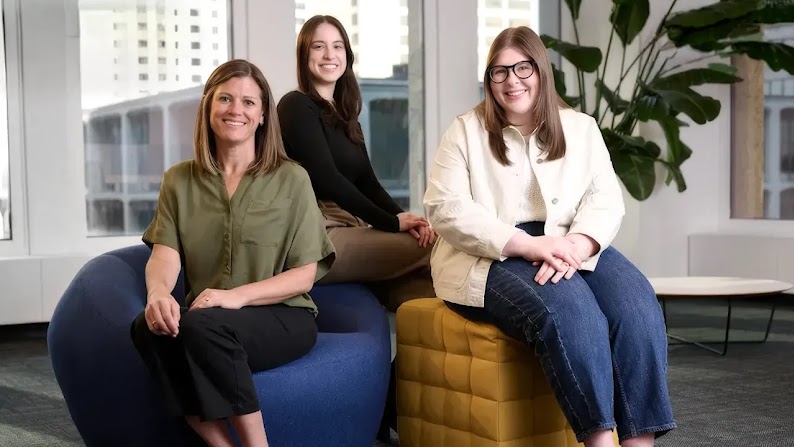 Wpromote lead-gen team members Alison Buchheit, Lexi Hoffman, and Amy Adams sit on comfortable office furniture in front of large windows.