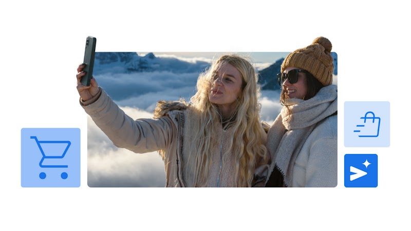 Duas mulheres brancas, uma loira e outra morena, tiram uma selfie no topo de uma montanha.