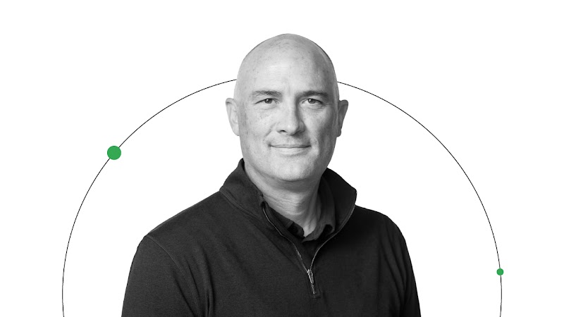 Brendon Kraham, VP of Search and Commerce Global Ads Solutions bei Google, ist auf dem Bild zu sehen und lächelt. Er hat helle Haut und trägt einen dunklen Pullover. Sein Porträt wird von einer schwarzen Linie mit zwei grünen Punkten eingerahmt.