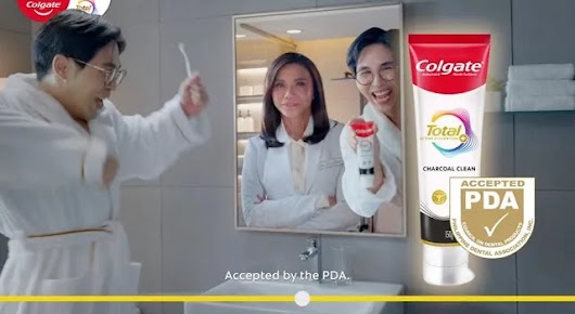 A Colgate video advertisement showing a man in a bathrobe looking at a mirror reflection of two people, with a large tube of Colgate Total and an 'Accepted PDA' seal on the right