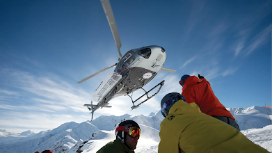 Image of a Heli Ski helicopter above a group of skiers on a mountain top.